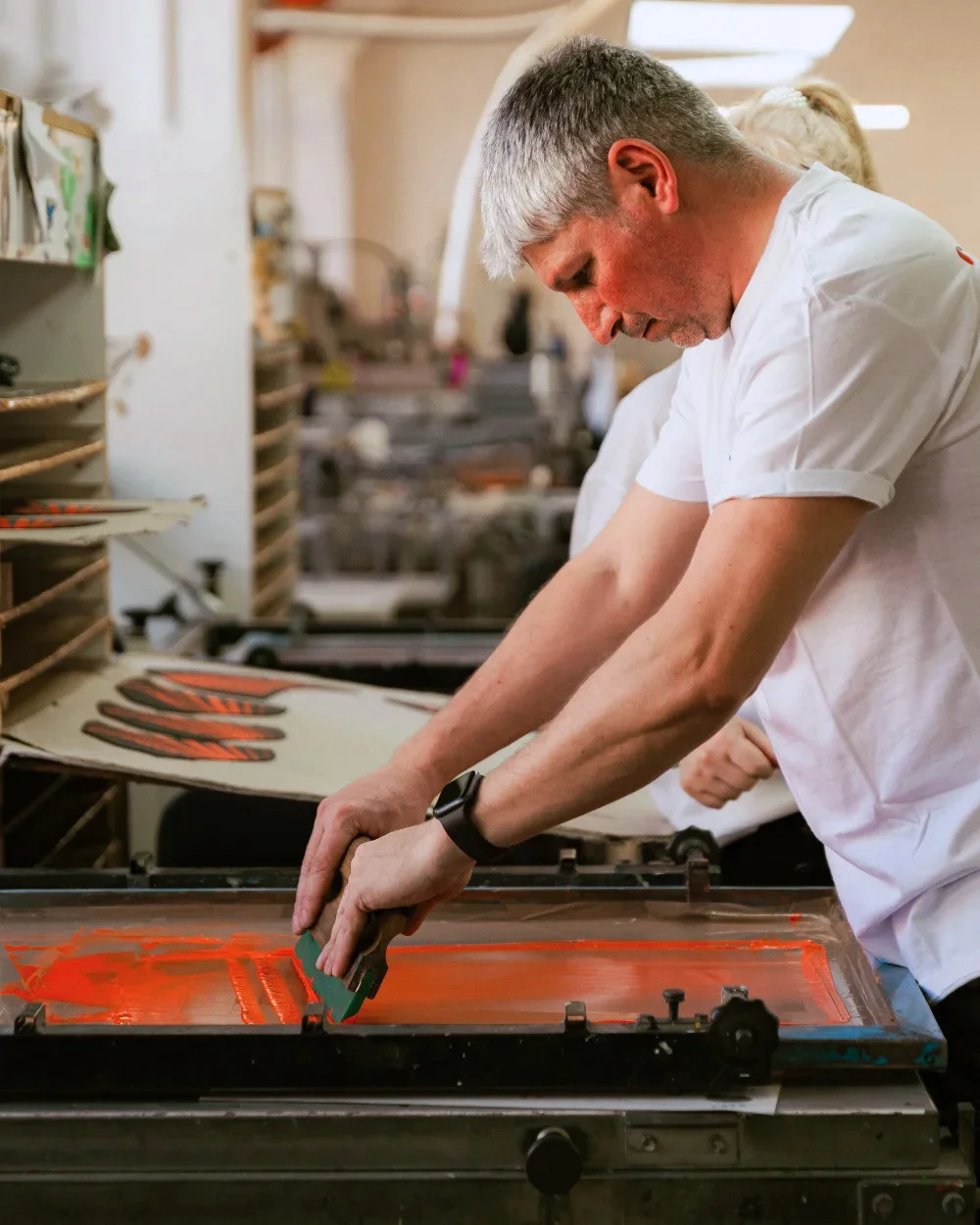 Operator trăgând cerneală portocalie pe ecran de serigrafie - Antel Print