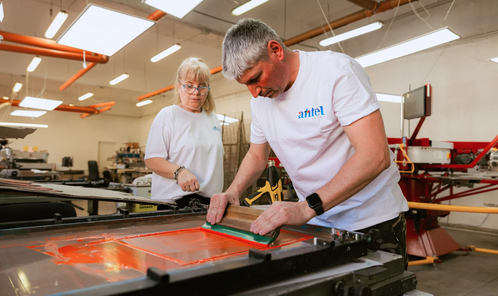 Operatori Antel Print trăgând cerneală portocalie pe ecran de serigrafie - Antel Print